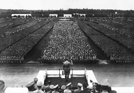 "Adolf Hitler discursando num comício do Partido Nazi em Nuremberga em 1934, demonstrando o poder da propaganda e mobilização de massas na Alemanha nazi."